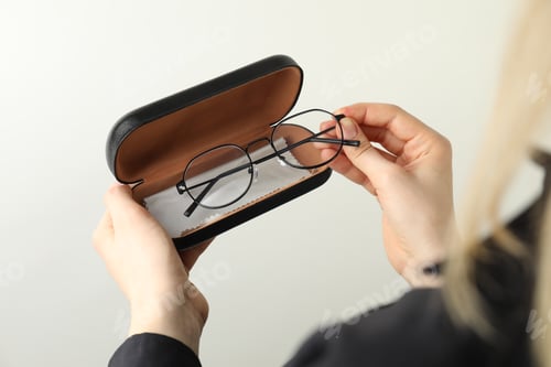 Preview: Woman holding case with stylish glasses and cleaning cloth on light background, closeup