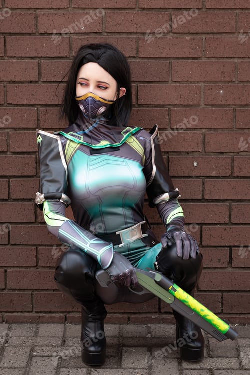 Preview: Female cosplayer in a green action suit against a brick wall