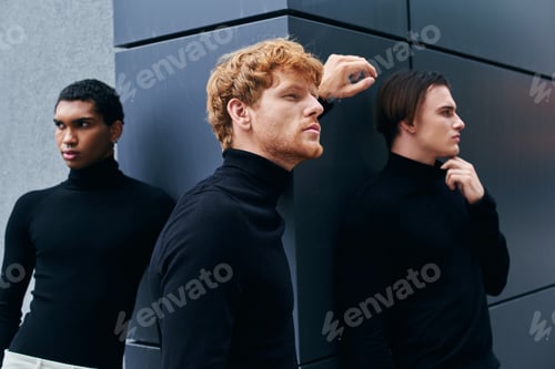 Preview: attractive pensive men in stylish black turtlenecks posing and looking away with wall backdrop