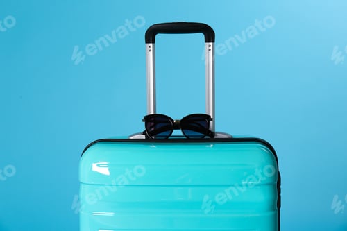 Preview: Stylish suitcase with sunglasses on color background