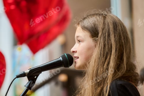 Preview: Young girl speaking into microphone with red heart balloons in background