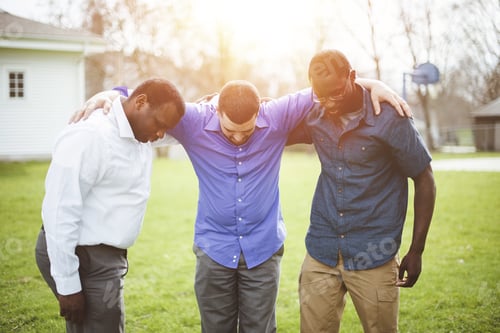 Preview: Group of diverse friends with hands on the shoulders looking down and praying together