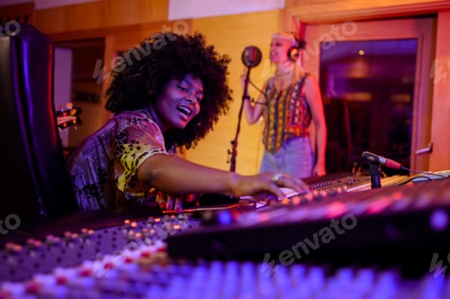 Preview: Multiracial music producer enjoying the recording of a female vocal, working on mixing console.