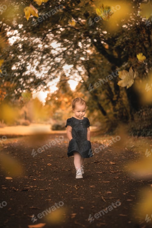 Preview: Little toddler girl walking with hands in pockets through autumn wonderland