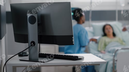 Preview: Hospitalized woman resting in bed while asisstant with black skin monitoring sickness symptom