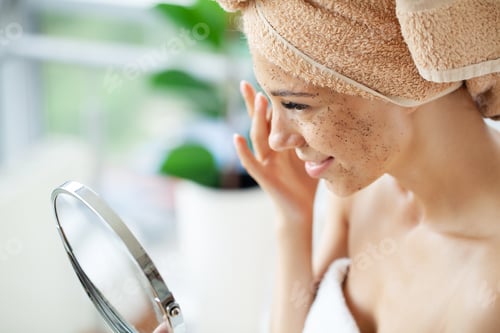 Preview: Close up of smiling woman applying coffee scrub on face