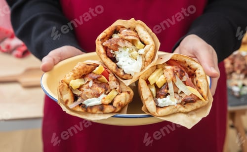 Preview: Gyro pita Shawarma, sliced meat tzatziki and vegetable wrap in male hand, close up view.