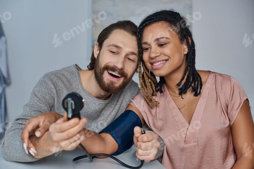 Preview: joyful man measuring blood pressure of pregnant african american wife, future parents, happiness