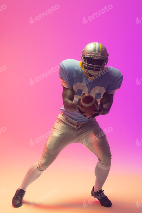 Preview: African american male american football player holding ball with neon pink lighting
