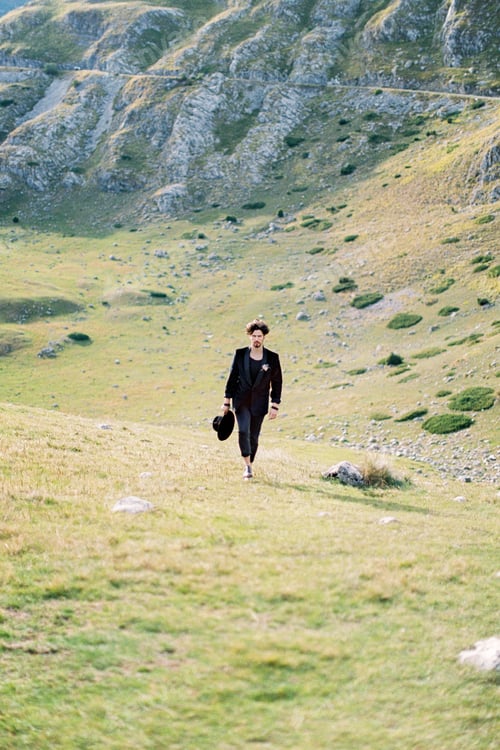 Preview: Man walks through a mountain valley with a black hat in his hand