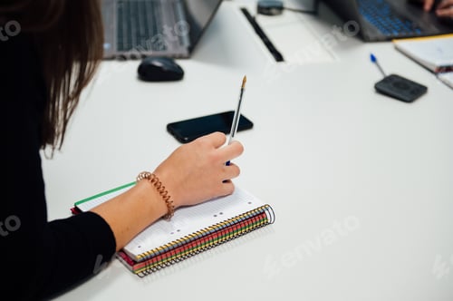 Preview: High-angle view of a woman's hand on her notebook taking notes during a meeting
