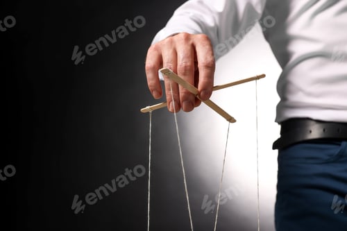 Preview: Man in formal outfit pulling strings of puppet on dark background, closeup. Space for text
