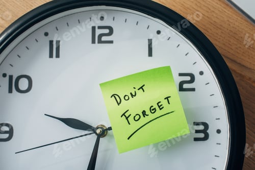 Preview: Top view of sticky note with dont forget lettering on clock on table