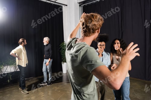 Preview: interracial actresses smiling near redhead man gesturing during rehearsing in acting skills school