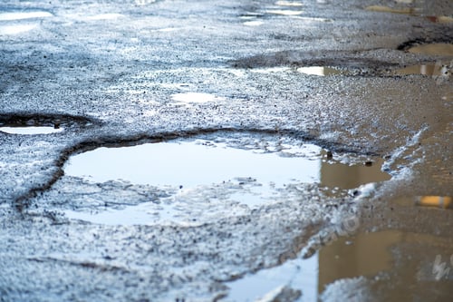 Preview: Close up of a road in very bad condition with big potholes full of dirty rain water pools.