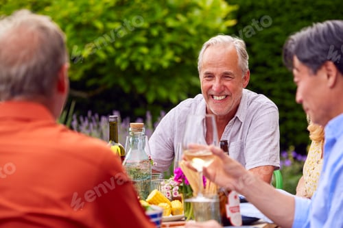 Preview: Group Of Mature Friends Talking Around Table At Summer Dinner Party In Garden At Home