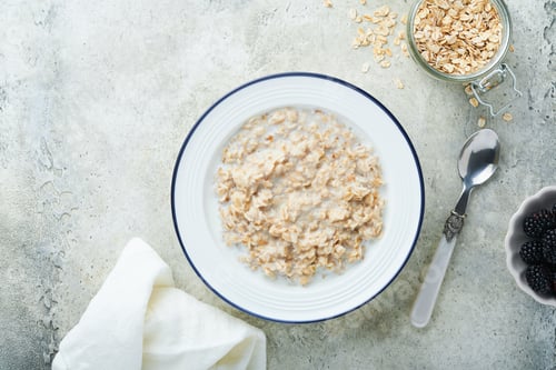 Preview: Oatmeal. Bowl of oatmeal porridge with strawberry, almond and milk on vintage light grey teal table.