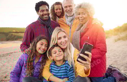 Preview: Multi-Generation Family Sitting By Fire On Winter Beach Vacation Taking Selfie