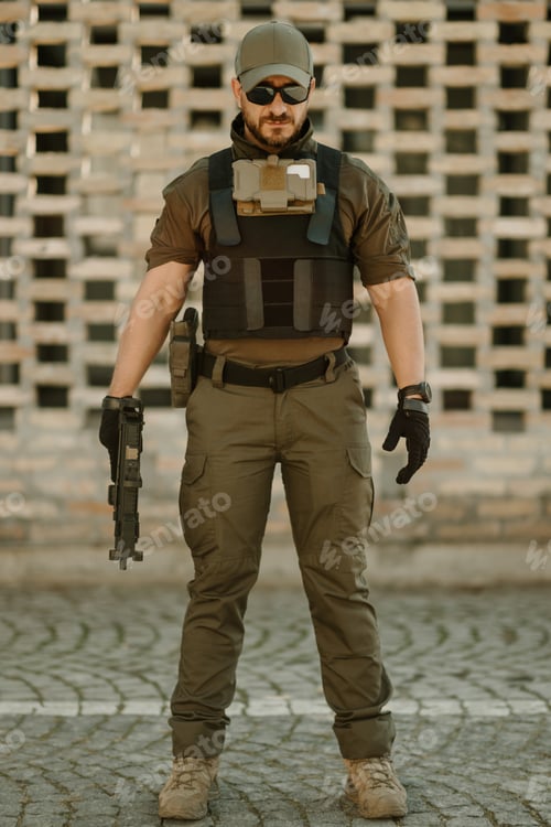 Preview: Soldier wearing tactical gear and holding a gun is standing in urban environment