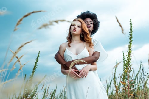 Preview: selective focus of african american woman hugging redhead girl against blue sky