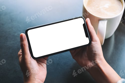 Preview: A woman holding black mobile phone with blank screen with coffee cup on the table