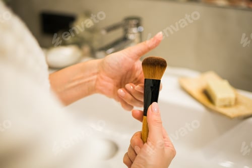 Preview: Female hand holds makeup brush in bathroom. Make-up artist profession concept. Variety of visagist