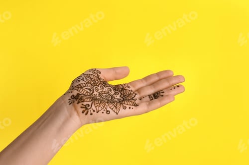 Preview: Woman with henna tattoo on palm against yellow background, closeup. Traditional mehndi ornament