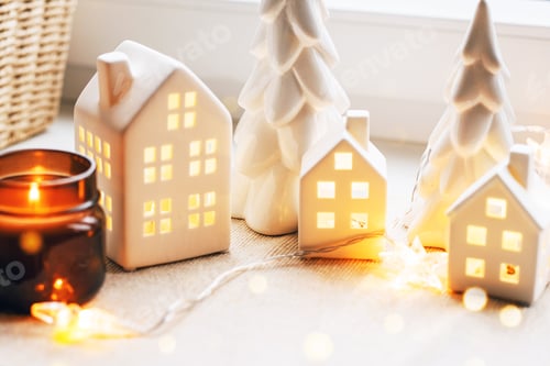 Visualização: Cena de Natal aconchegante com casas de cerâmica e luz de velas perto de uma janela