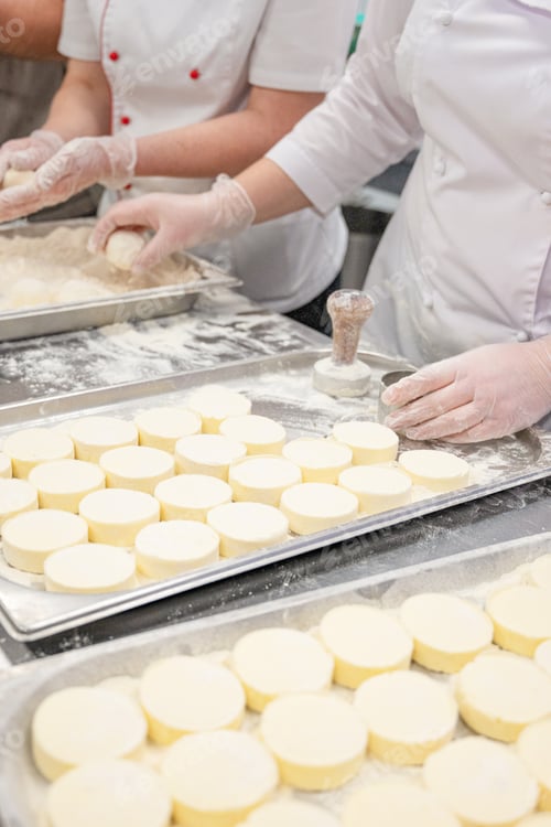 Preview: Chefs in uniform prepare cottafe cheese or syrniki on metal trays sprinkled with flour