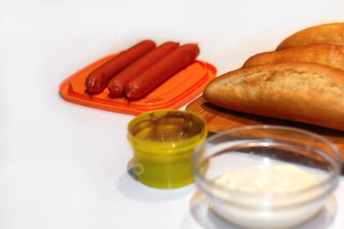 Preview: ingredients for making homemade hot dogs. Sausages in orange plate, fresh baked buns, mustard and sa