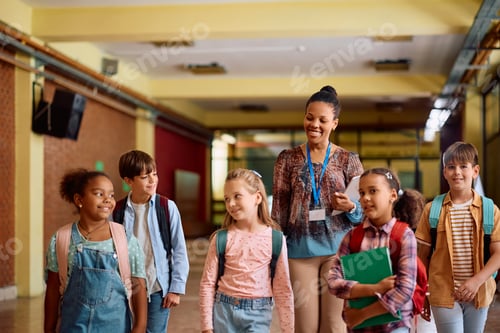 Visualização: Professora negra feliz e seus alunos do ensino fundamental caminhando pelo corredor da escola.