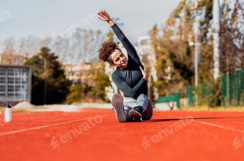 Preview: Young woman stretching her muscles before running on sport track outdoors.