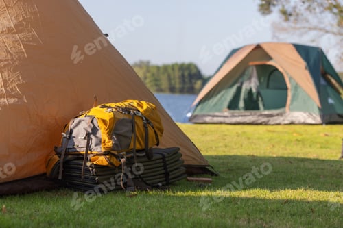 Preview: A yellow backpack sits outside a tent on a grassy lakeside campsite.