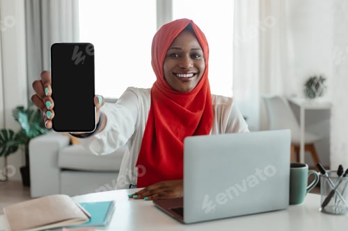 Preview: Happy black muslim woman with laptop showing smartphone with blank screen, recommending app, mockup