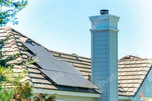 Preview: Chimney on a brown tile roof with solar panels on it under a clear sky on a sunny da