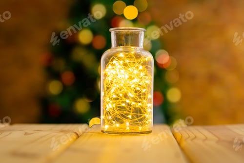 Preview: Composition of fairy lights in vase on wooden table with christmas tree and lights in background