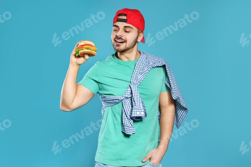 Preview: Handsome man with tasty burger on color background