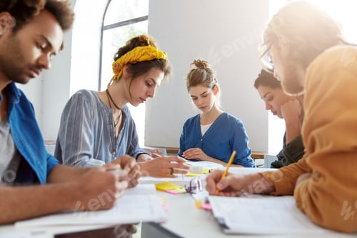 Preview: Portrait of five students of different races preparing for lessons at university making notes on pap