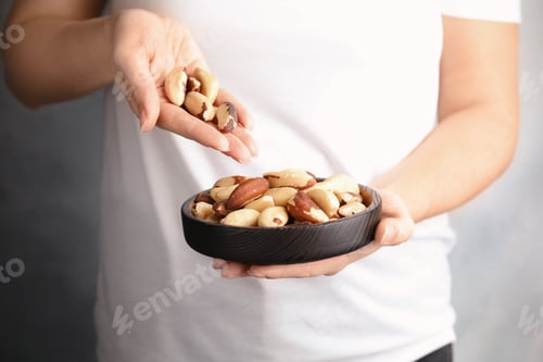 Preview: Woman with Brazil nuts on grey background, closeup