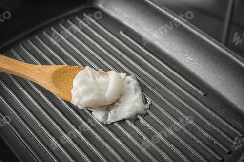Preview: Wooden spoon with coconut oil in frying pan, closeup. Healthy cooking