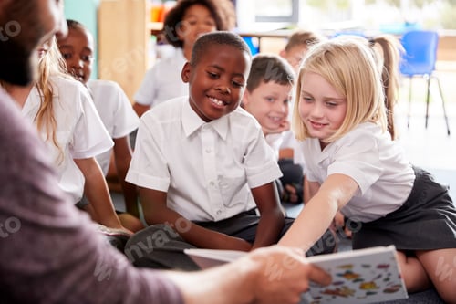 Preview: Male Teacher Reading Story To Group Of Elementary Pupils Wearing Uniform In School Classroom