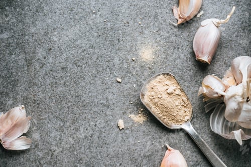 Preview: top view of several ripe cloves of garlic and spice in metal spoon on grey background