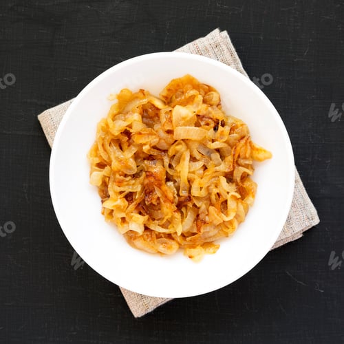 Preview: Homemade caramelized onions on a white plate on a black surface, top view.