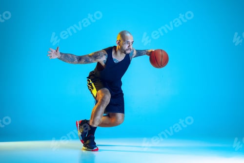 Preview: Young basketball player training isolated on blue studio background in neon light
