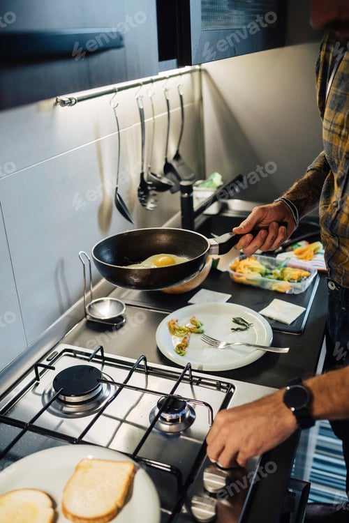 Preview: Mid adult man preparing fried eggs at kitchen hob, cropped