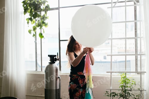 Preview: Young woman attaching bunting to balloon in design studio