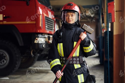 Preview: With hammer in hands. Female firefighter in protective uniform standing near truck