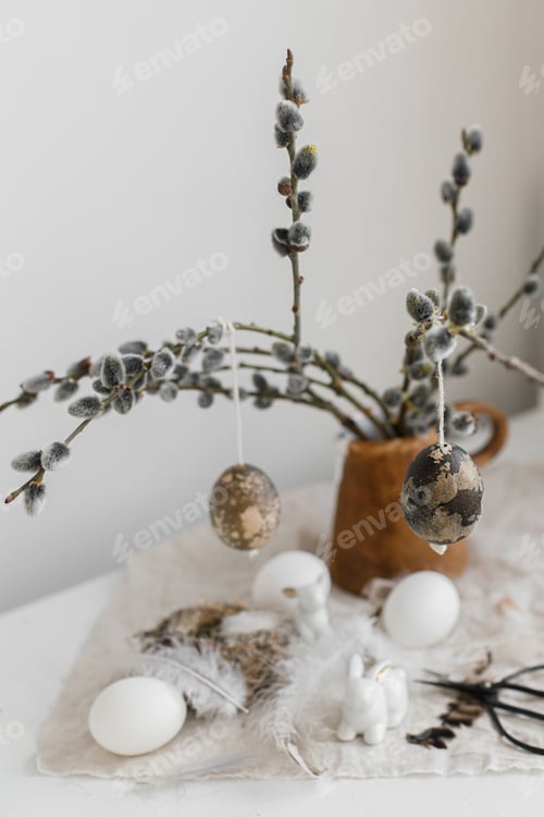 Preview: Happy Easter! Natural eggs, bunny figurines, feathers, nest, willow branches in vase on table