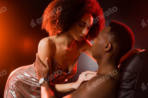 Preview: curly african american woman in dress seducing shirtless man on black background