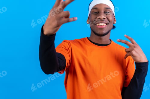 Preview: Black ethnic man in orange clothes on a blue background, having fun and dancing